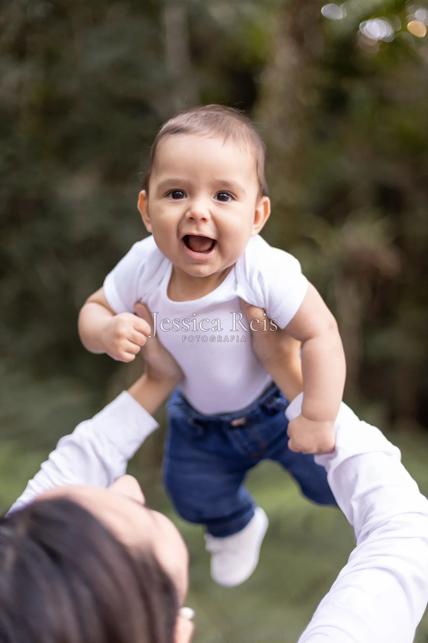 Pai lançando o bebê ao alto na brincadeira, ensaio de família ao ar livre