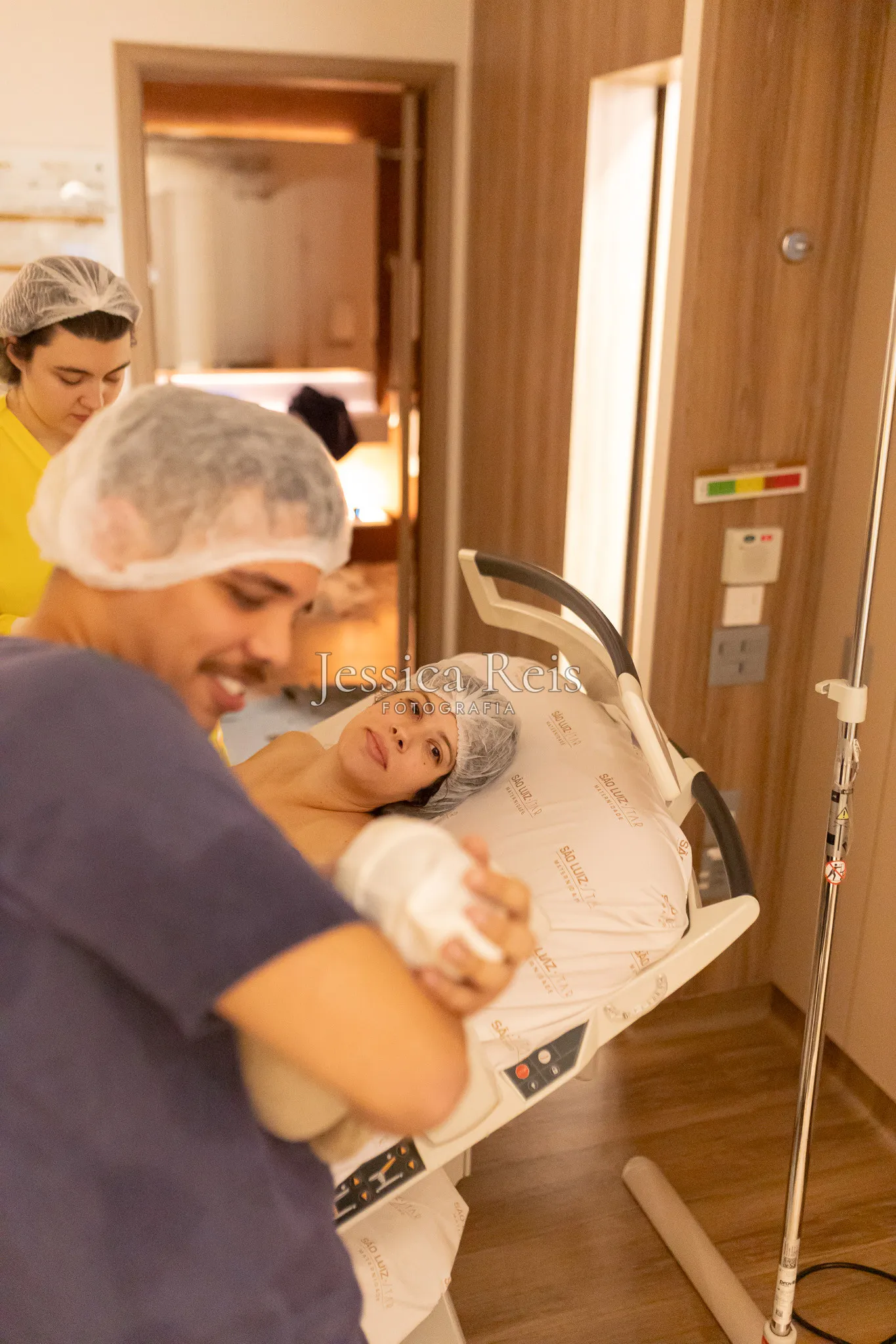Pai segurando o bebê recém-nascido após parto normal com a mãe observando, na Maternidade São Luiz Star