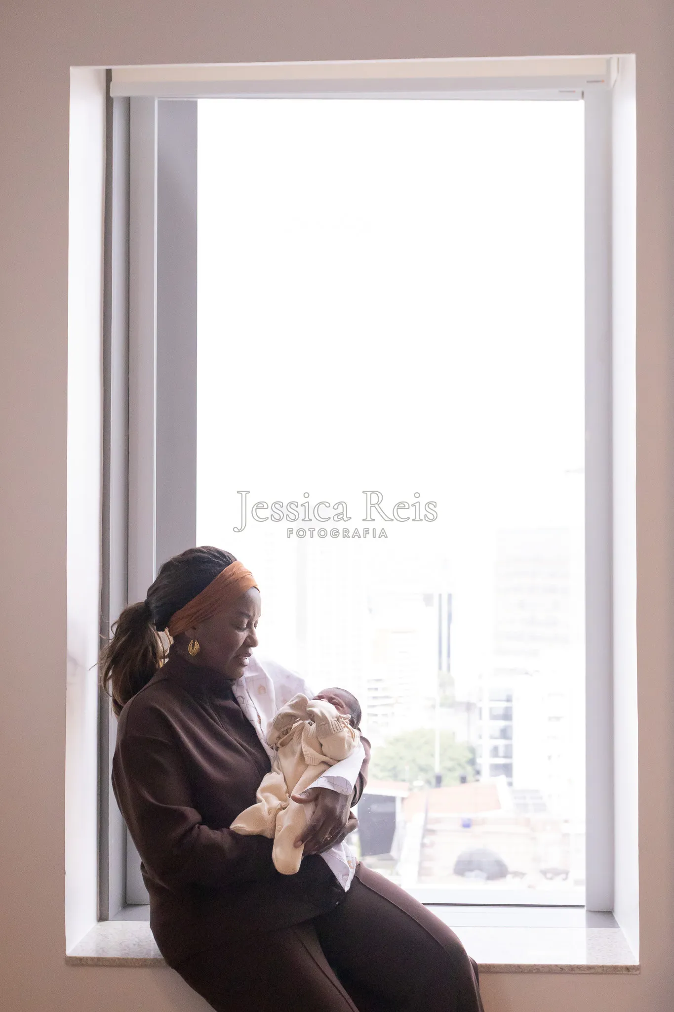 Avó com a bebê no colo diante da janela, ensaio  fresh 24h na maternidade São Luiz Star em São Paulo