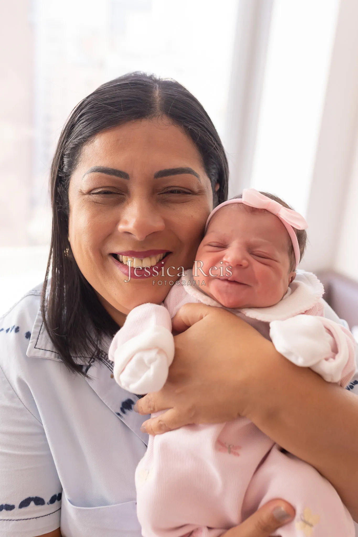 Avó sorrindo com a recém-nascida no colo, ensaio pós-parto na maternidade em luz natural